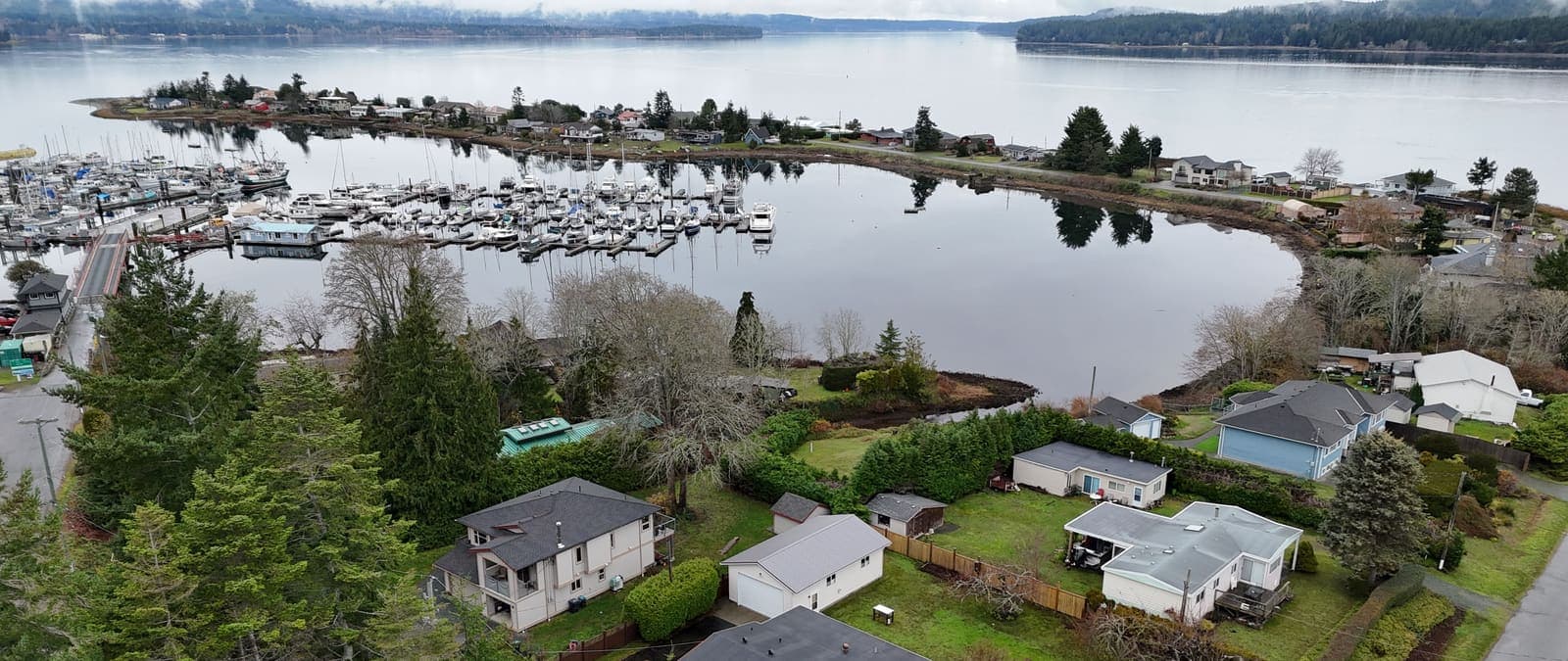 Aerial view of a sheltered east coast Vancouver Island harbour with a marina, moored boats and a low residential shoreline