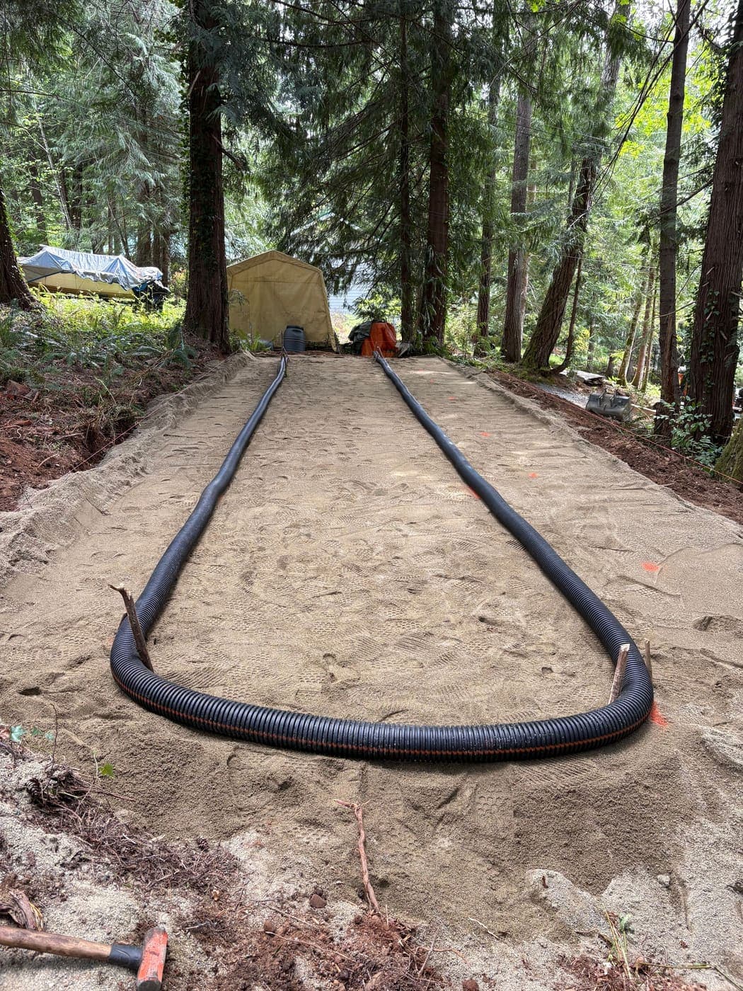Sand lined seepage bed under construction, showing the levelled specification sand layer with two black perforated passive vent runs laid along the outside edges