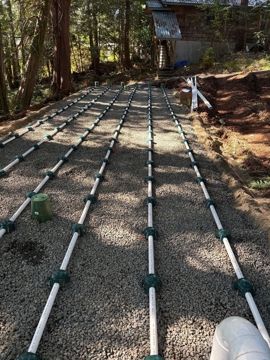 Six white PVC pressure distribution laterals laid in washed pea gravel across a sand lined bed, each orifice covered by a green shield