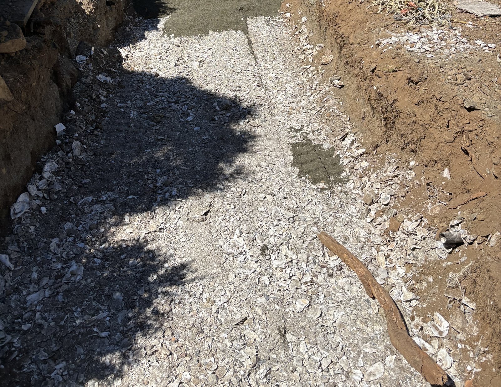 A layer of crushed oyster shell spread across the floor of an excavated dispersal bed, with sand starting to be placed over it at the far end
